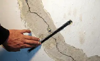 A wall with a large crack is being inspected by a professional in Phoenix, AZ